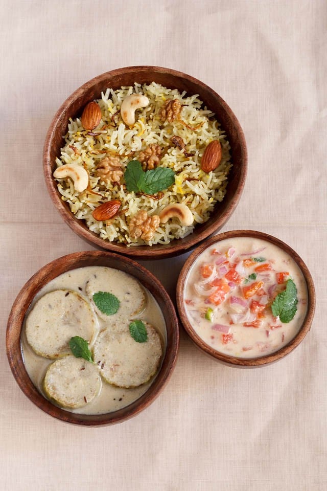 onion tomato raita garnished with mint leaf and served in a bowl with pulao and side dish
