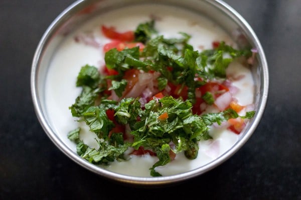 adding chopped mint leaves and chopped green chili to curd for onion tomato raita