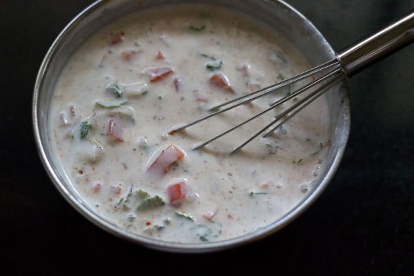 mixing ingredients to make onion tomato raita 