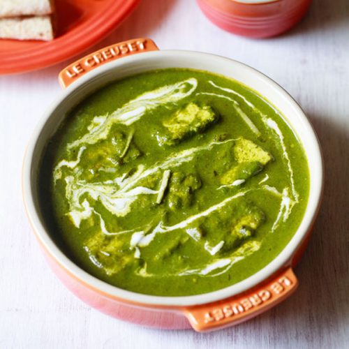 palak paneer topped with cream, garnished with ginger julienne and served in an orange bowl on a white board