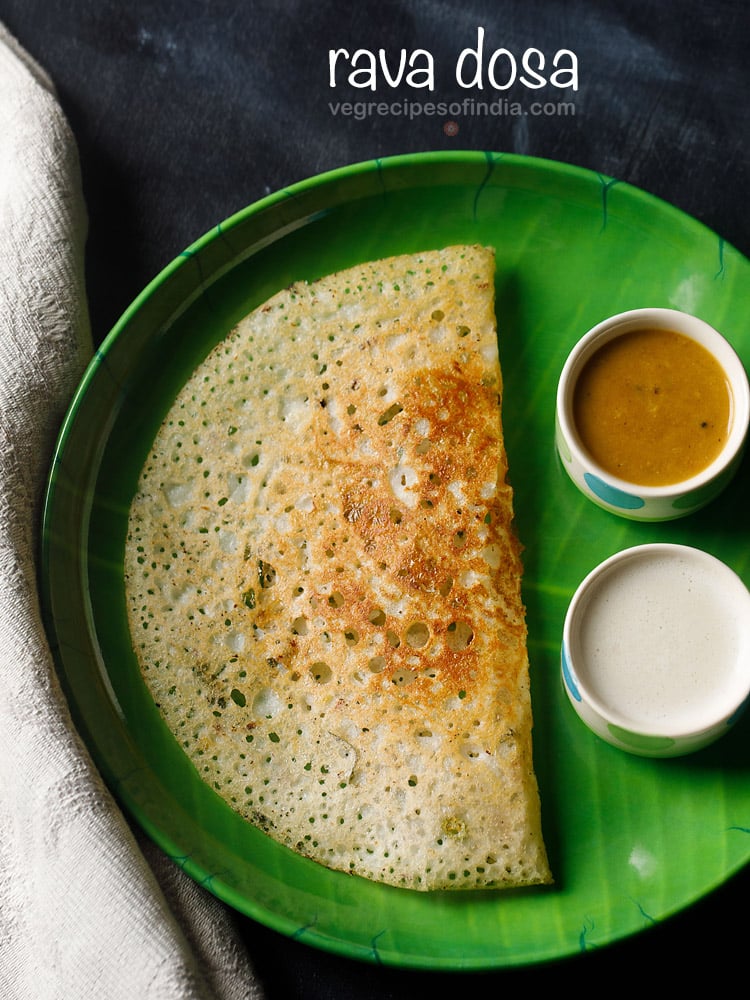 rava dosa served in a green plate with a side of two bowls having sambar and coconut chutney on a dark black-blue board