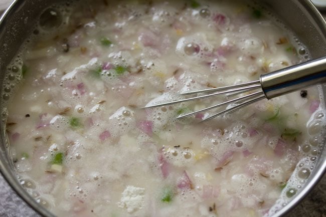 mixing the ingredients with a wired whisk to make suji ka dosa batter.