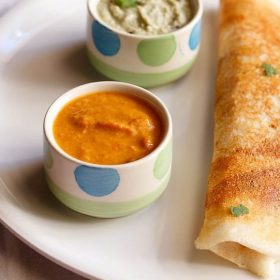 red chutney for dosa served in a bowl kept on a plate with mysore masala dosa kept on right side and coconut chutney in another bowl.