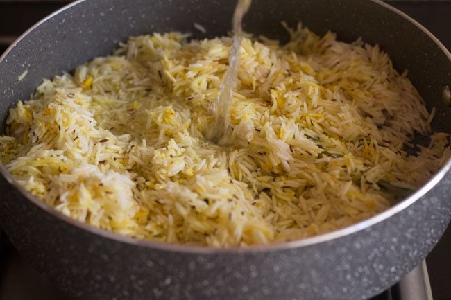 adding water to the rice in the pan