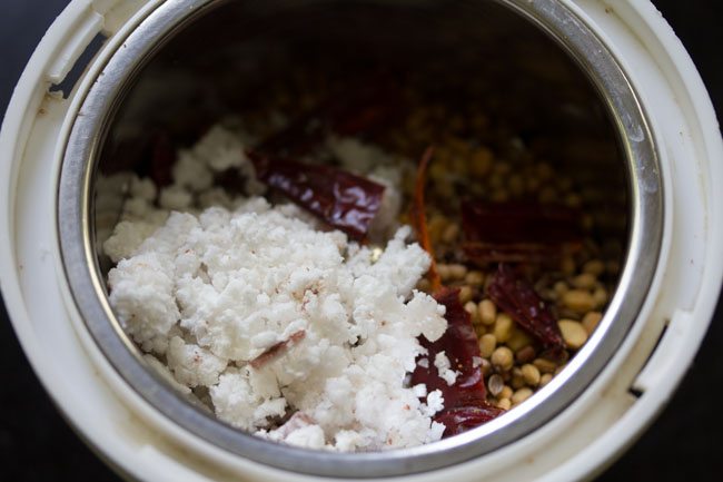 adding roasted spices in grinder jar along with water and coconut for udupi sambar powder