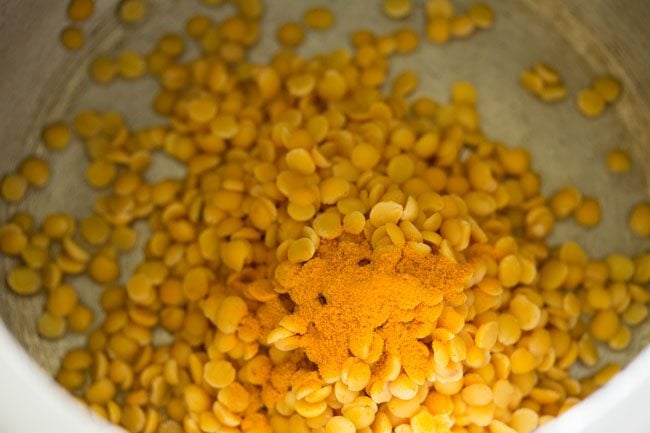 adding tuvar dal and turmeric powder in pressure cooker for udupi sambar