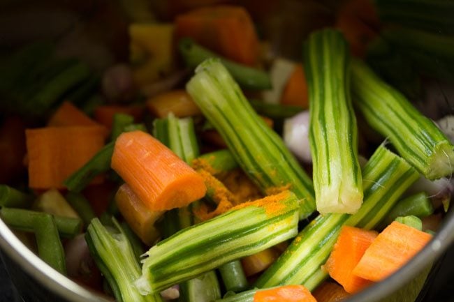 adding sambar onions, carrot, bottle gourd, brinjal, drumsticks, curry leaves and turmeric powder in pan for udupi sambar