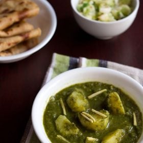 aloo palak garnished with ginger julienne in a white bowl on a blue green white cotton napkin.