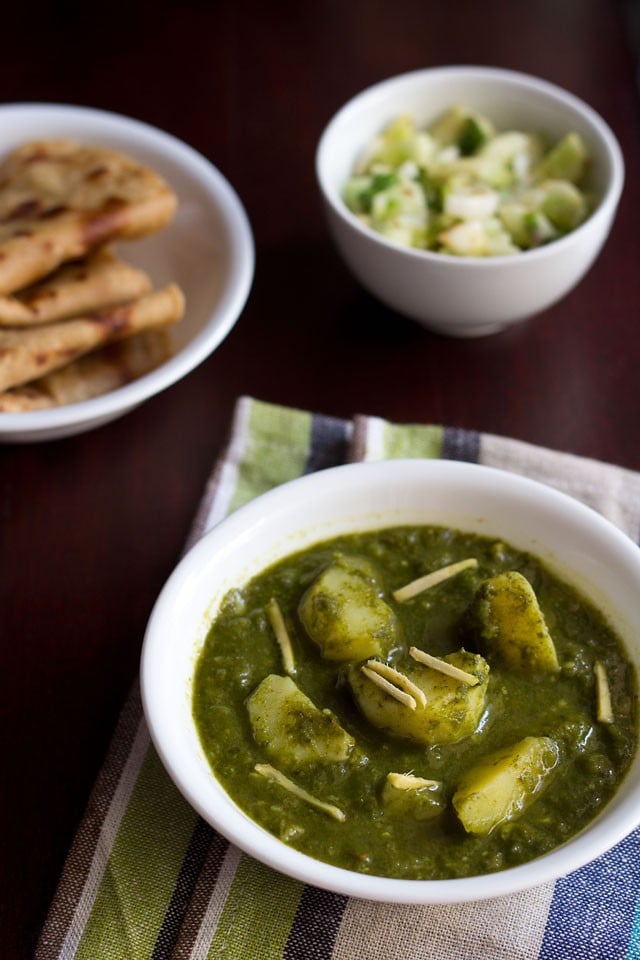 aloo palak garnished with ginger julienne in a white bowl on a blue green white cotton napkin.