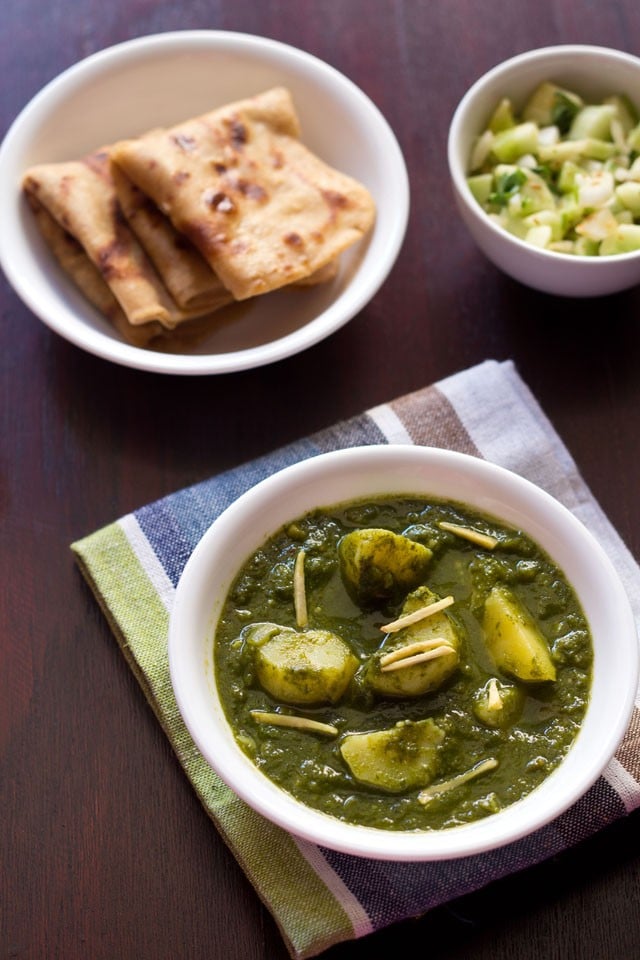 aloo palak garnished with ginger julienne in a white bowl on a blue green white cotton napkin