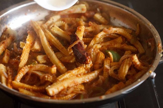 adding apple cider vinegar to baby corn jalfrezi in pan