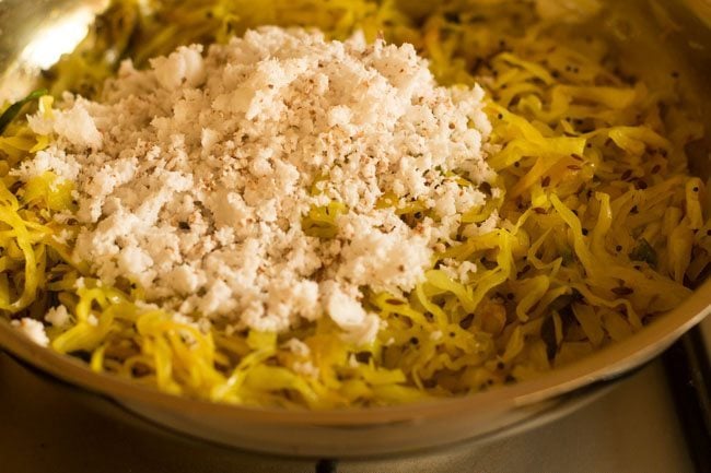 adding grated coconut to cooked cabbage in pan to make cabbage thoran recipe