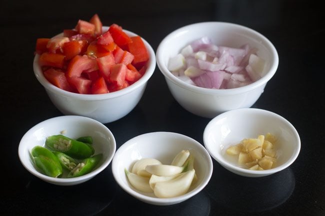 prepped up ingredients in white bowls - chopped onions, tomatoes, green chillies, garlic and ginger