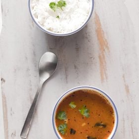 paruppu rasam garnished with coriander leaves and served in a bowl with rice on side.