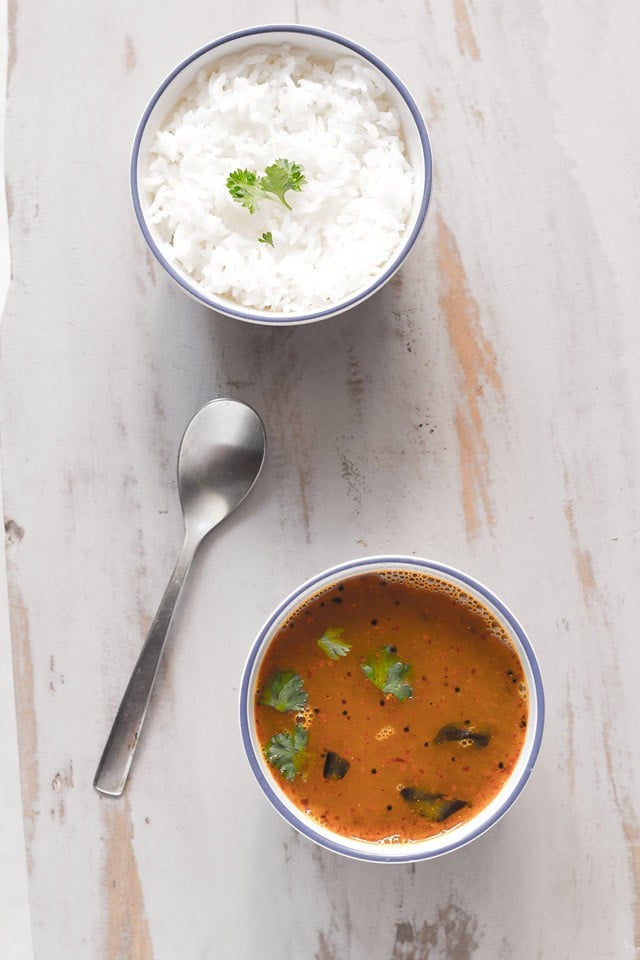 paruppu rasam garnished with coriander leaves and served in a bowl with rice on side.