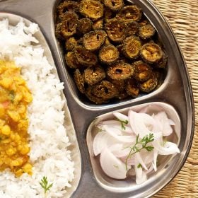 karela fry or bitter gourd fry or Kakarakaya fry served in a steel plate with steamed rice, onion slices, dal and a glass of water