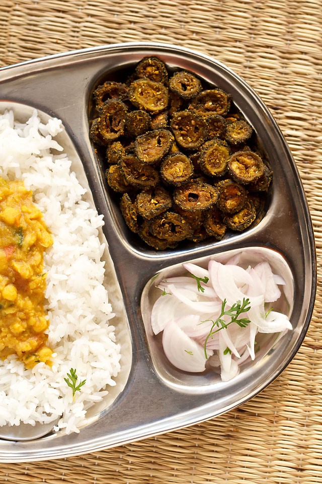 karela fry or bitter gourd fry or Kakarakaya fry served in a steel plate with steamed rice, onion slices, dal and a glass of water