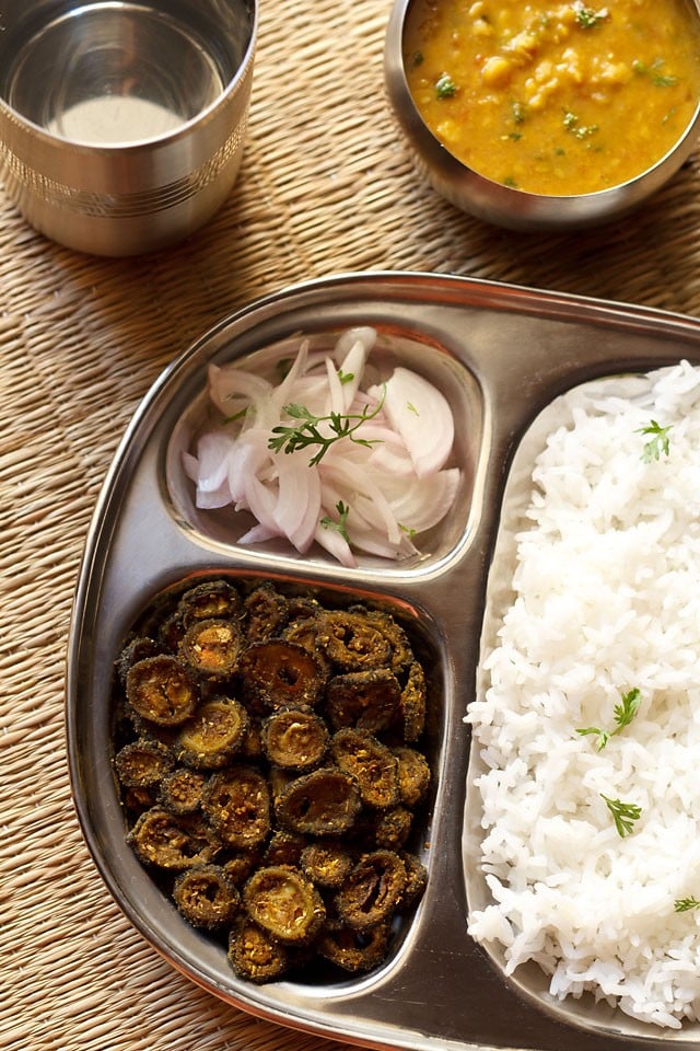 karela fry served in a steel plate with steamed rice, onion slices, dal and a glass of water 