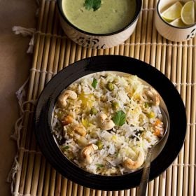 kashmiri biryani in a bowl on bamboo mat with raita and lemons in two bowls