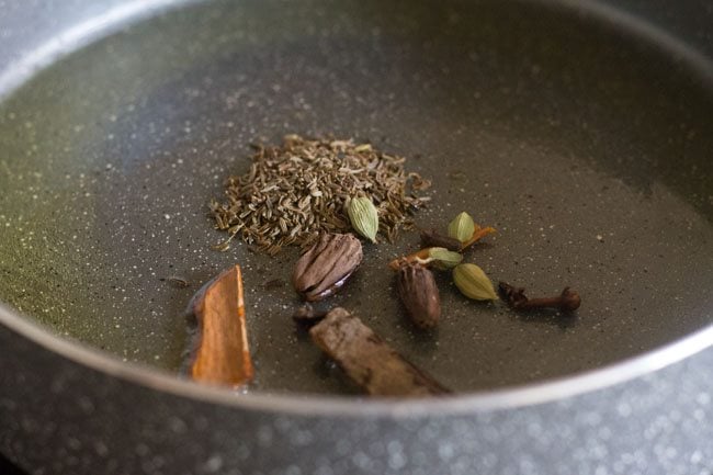 adding caraway seeds, cinnamon, black cardamoms, green cardamoms, cloves and mace to the pan