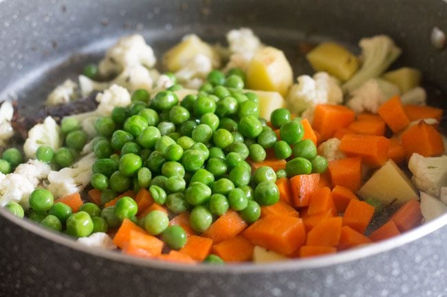 adding chopped vegetables to the pan - cauliflower, carrots, potatoes and green peas 