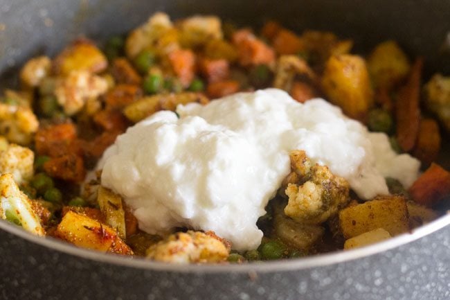 adding beaten yogurt to the vegetables in the pan