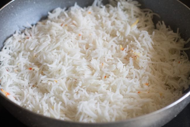 layering half the cooked rice on top of the vegetable gravy in the pan