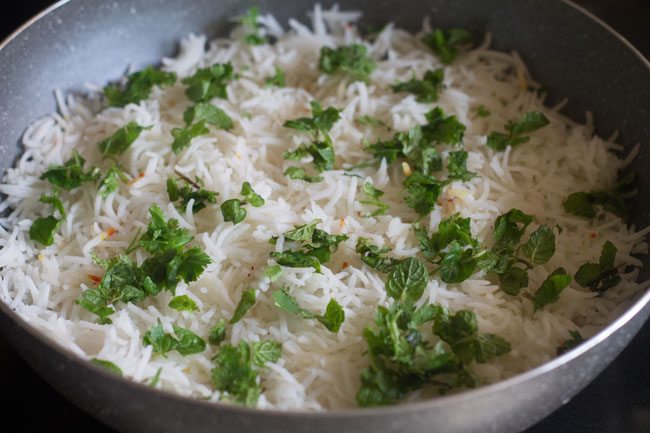 adding chopped mint leaves and chopped coriander leave son top of the rice in the pan