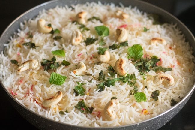 garnishing kashmiri biryani with roasted cashewnuts and some mint leaves 