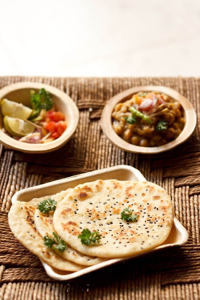 kulchas garnished with coriander and served on a plate with chole masala and salad 