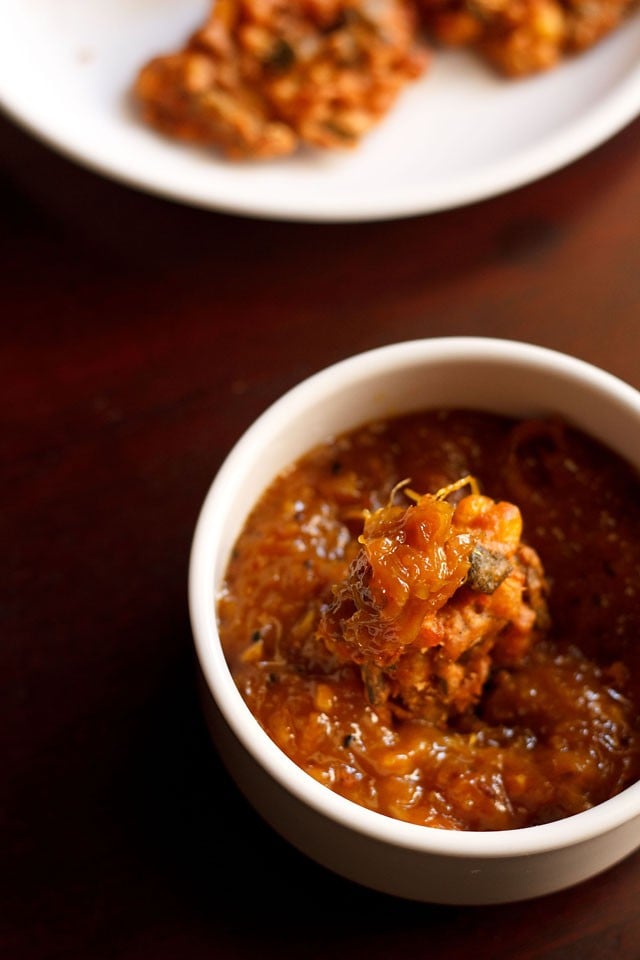 mango chutney in a white bowl with a pakora dipped inside the chutney