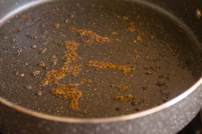 adding cumin seeds to hot oil in pan