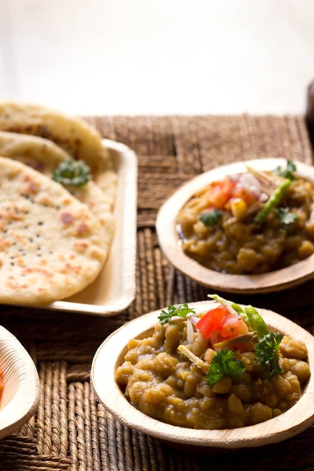 matar curry garnished with chopped onion, tomato, ginger, green chili, coriander leaves and served in bowls with kulchas on plates 