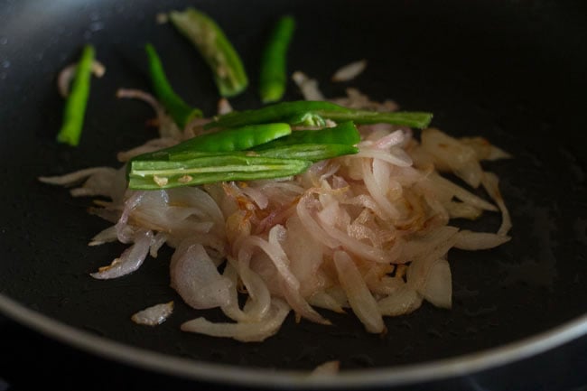 adding slit green chilies to the onions in pan