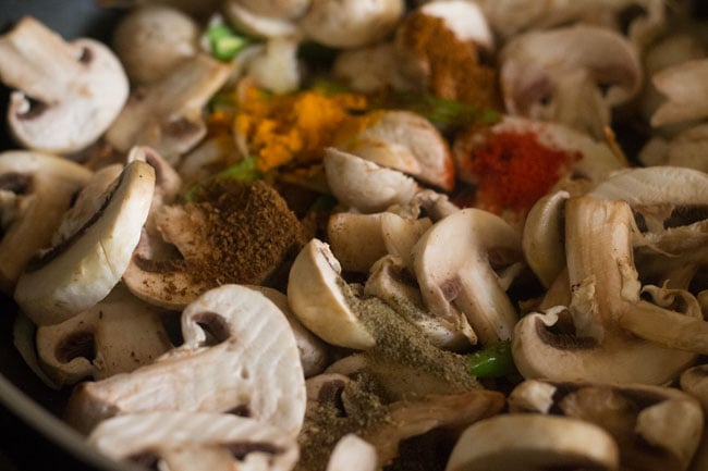 adding cumin powder, turmeric powder, black pepper powder, red chili powder, garam masala powder and salt to the mushroom mixture in pan