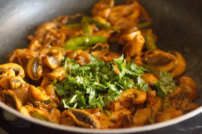 adding chopped coriander leaves to the mushroom fry in pan