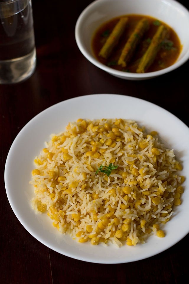 chana dal khichdi served on a white plate with drumstick curry.