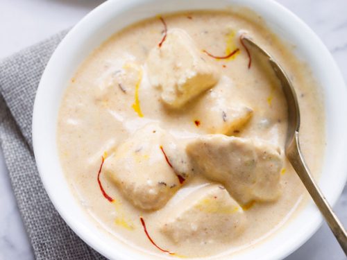 shahi paneer topped with some saffron strands and served in a white bowl with a spoon