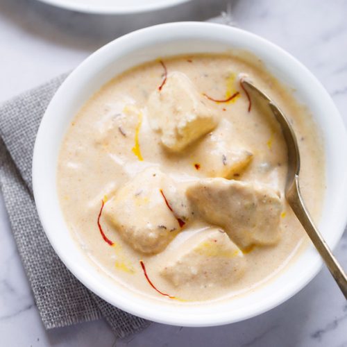 shahi paneer topped with some saffron strands and served in a white bowl with a spoon