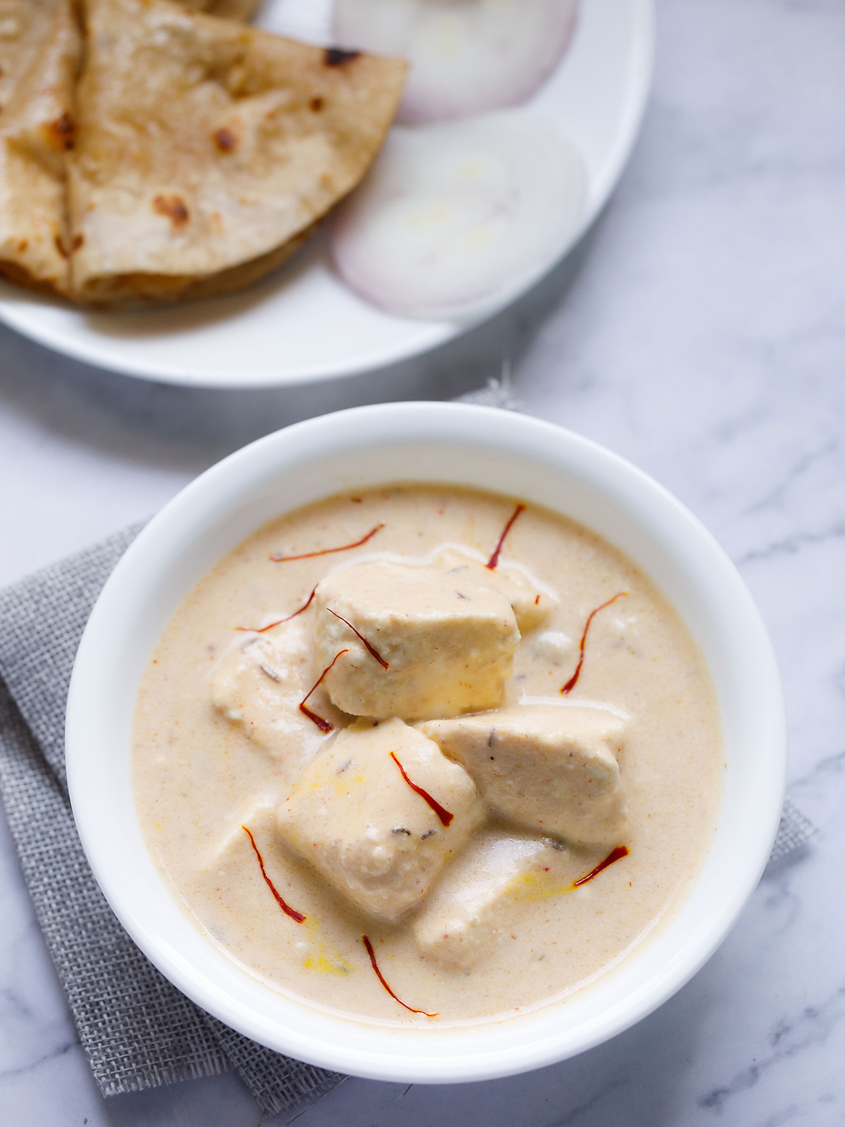 shahi paneer topped with some saffron strands and served in a white bowl on a white marble surface