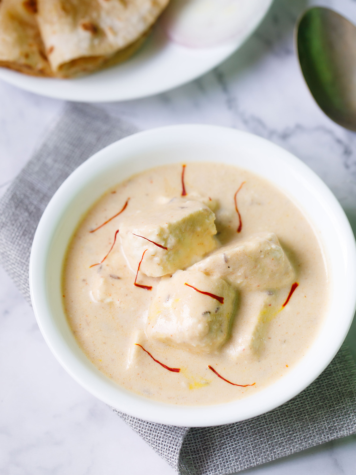 shahi paneer topped with some saffron strands and served in a white bowl on a white marble surface