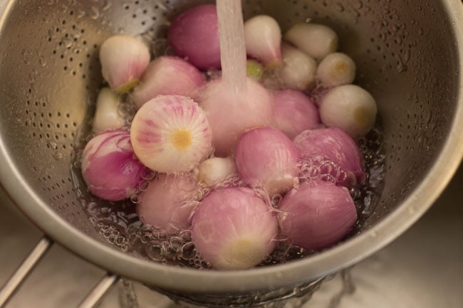 rinsing peeled small red onions in water in a strainer