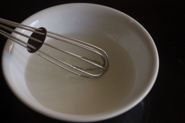 mixing vinegar-water mixture in the bowl with a wired whisk to make pickled onions recipe