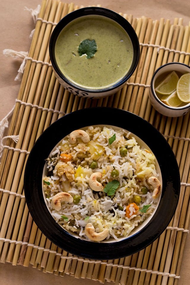 kashmiri biryani served in a bowl with raita and lemon wedges 