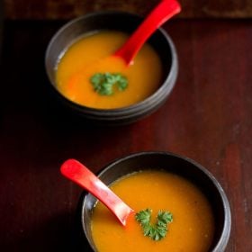 tomato carrot soup garnished with parsley and served in bowls with a red soup spoon.