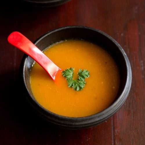 tomato carrot soup garnished with a parsley in a black bowl with a red soup spoon.