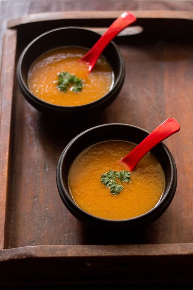 tomato carrot soup garnished with parsley and served in bowls with a soup spoon