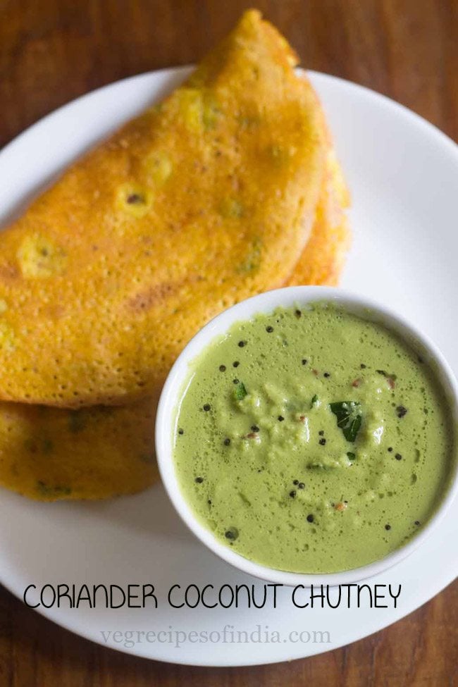 green coconut chutney served in a bowl with a dosa placed on a white plate and text layover. 
