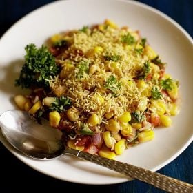 corn chaat served on a white plate with a spoon in it.