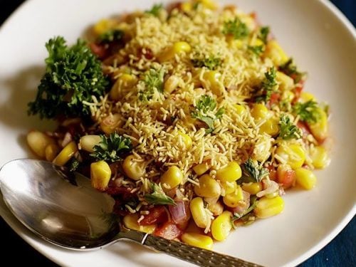 corn chaat served on a white plate with a spoon in it.